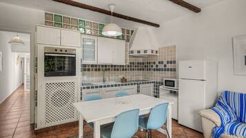 A compact kitchen with white cabinets, a dining table with chairs, a microwave, and a refrigerator.