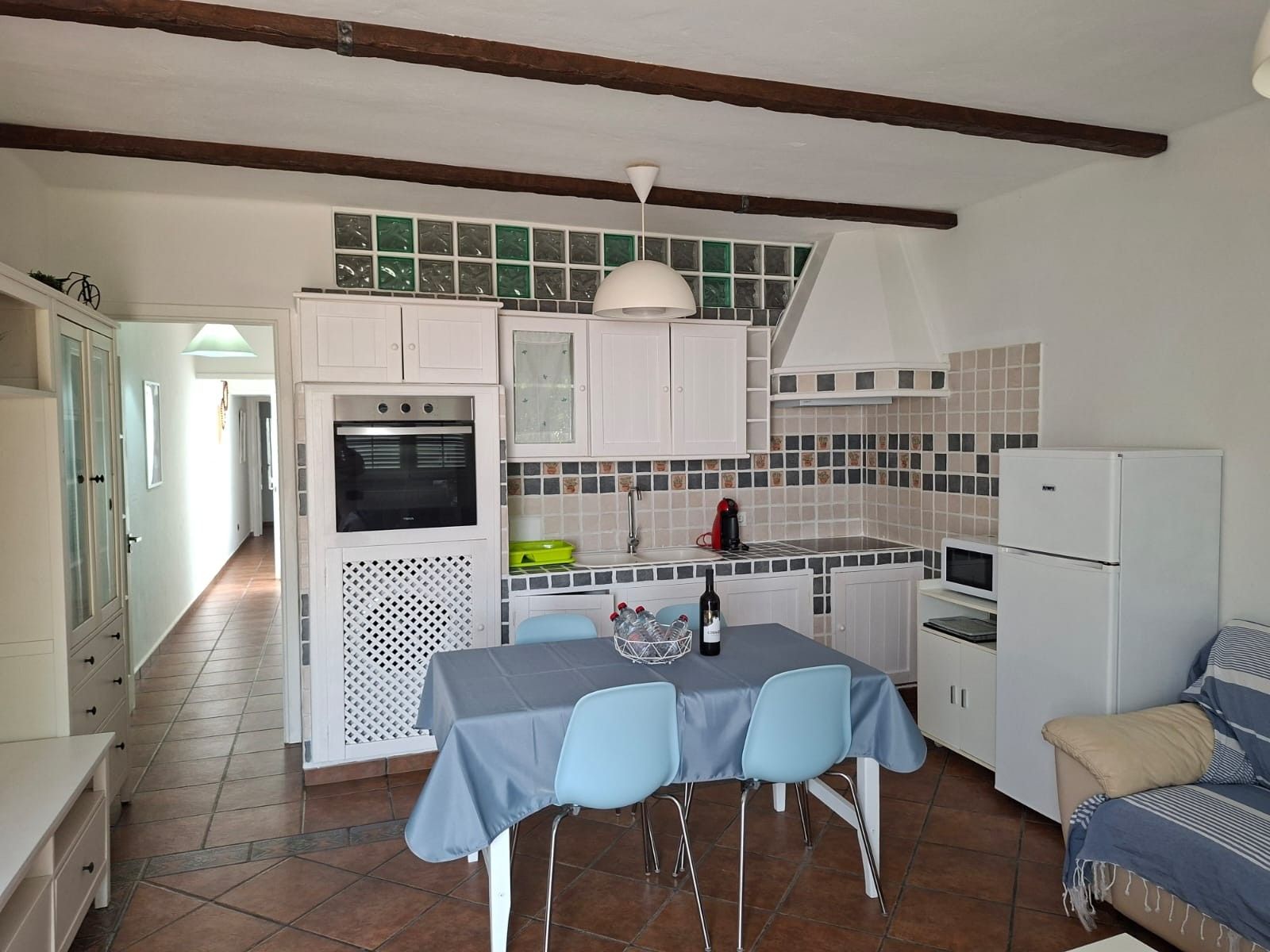 Cocina compacta con armarios blancos, horno integrado, cafetera y refrigerador.