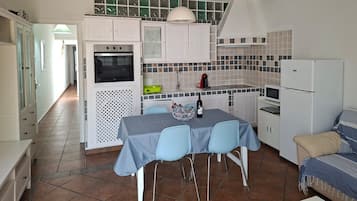 Cocina compacta con armarios blancos, horno integrado, cafetera y refrigerador.