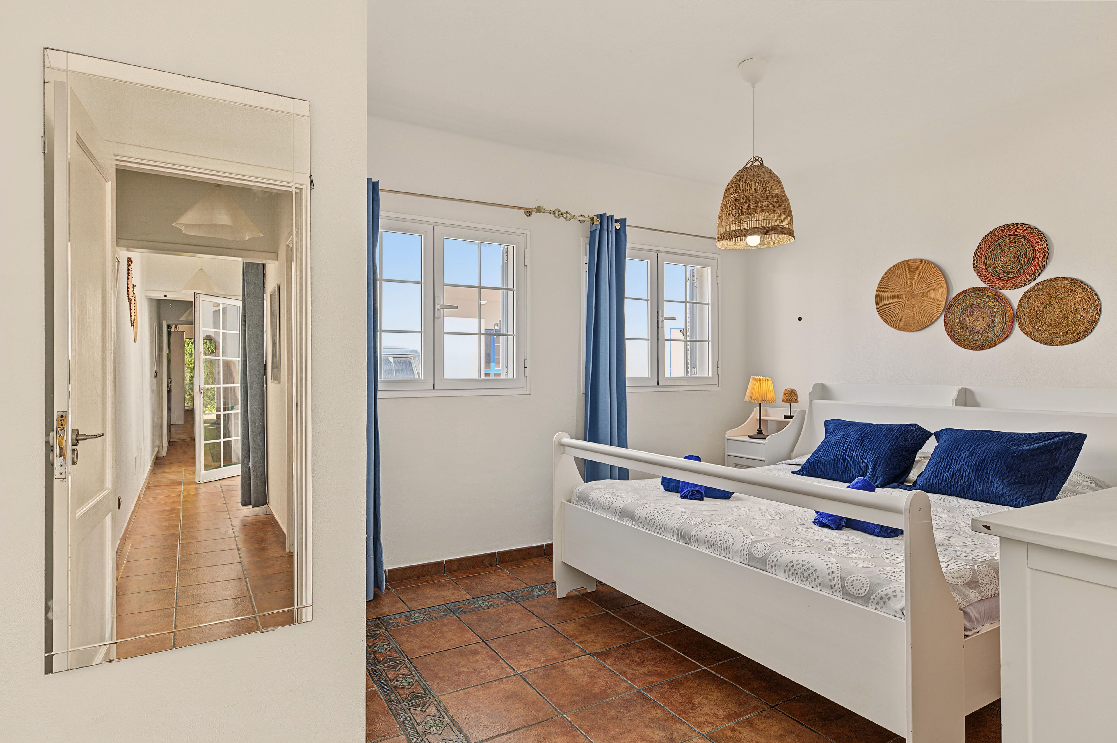 A bedroom with a bed, a window, a door, and a hanging light fixture.