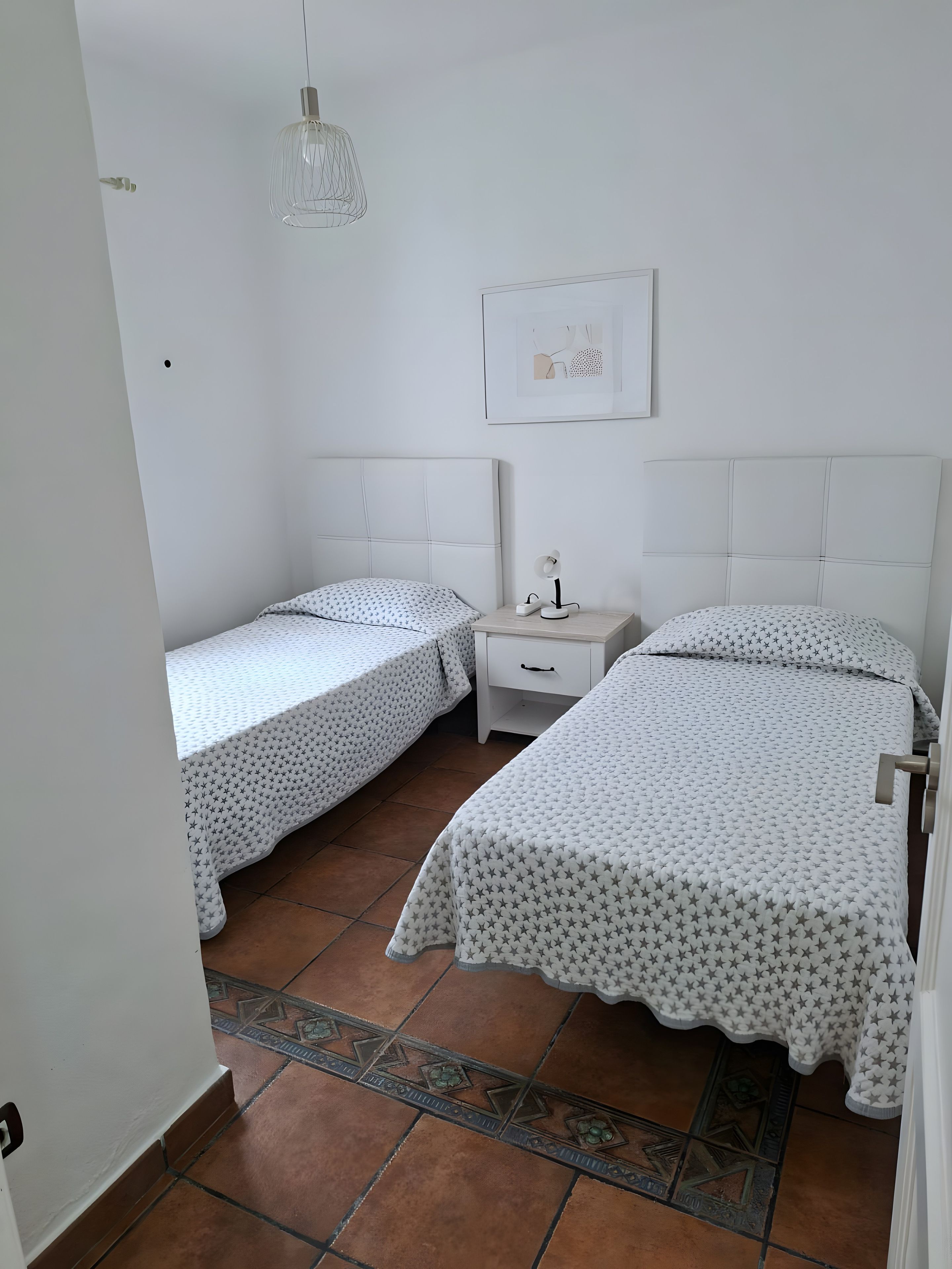 Un dormitorio con dos camas individuales, una mesita de noche, una lámpara y un cuadro enmarcado en la pared.