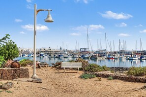 Praia arenosa com um banco e um poste de luz, com vista para um porto com vários barcos.