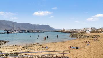 A coastal beach with boats, a rocky shoreline, and buildings in the background.