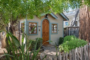 A house with a wooden door, number 1125, surrounded by greenery and a wooden fence. - 4090 Oceans of Time - Stunning Carmel Cottage (Carmel-by-the-Sea)