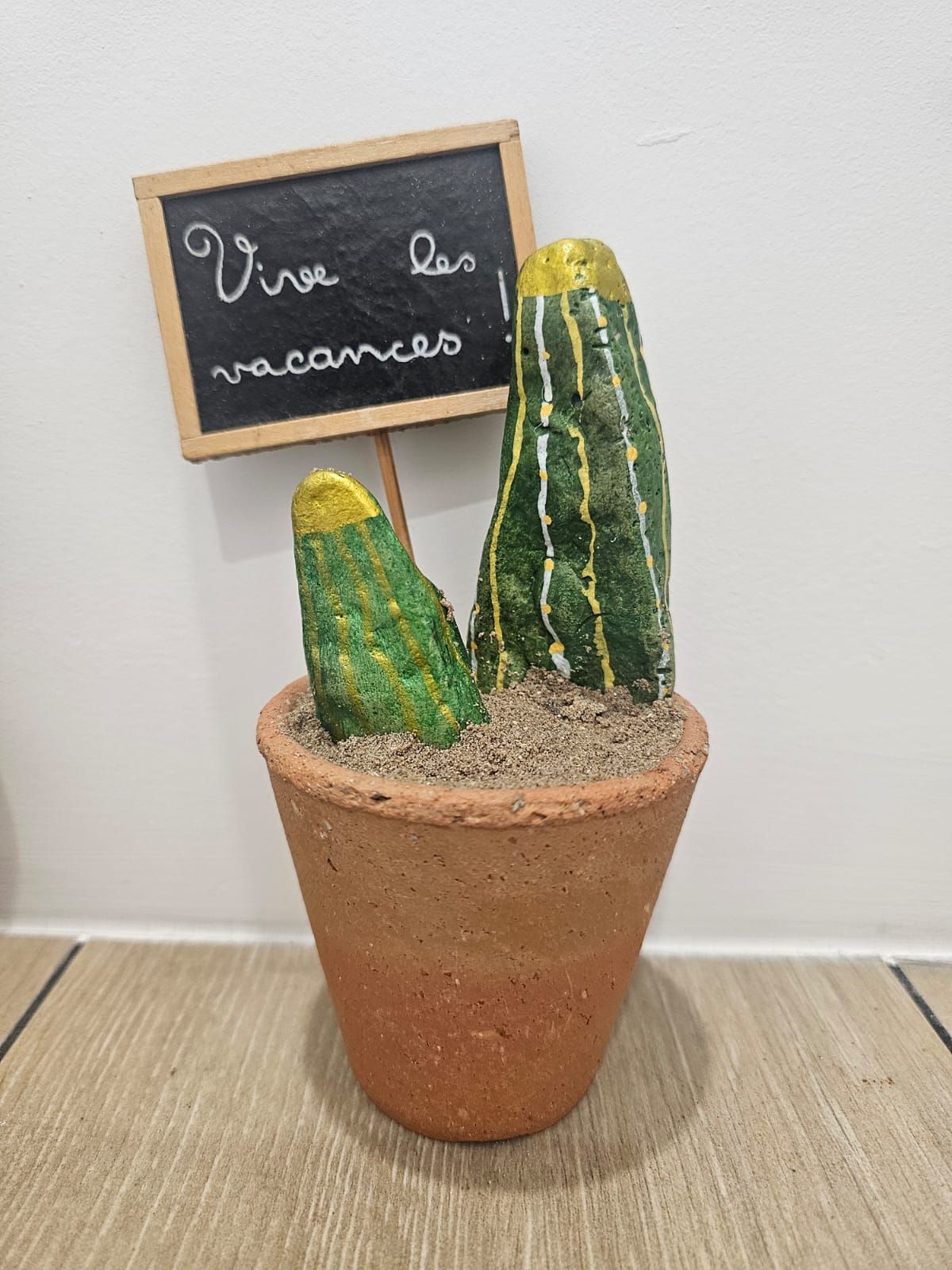 A terracotta pot with two cacti and a chalkboard sign with the text 'Vive las vacaciones'.