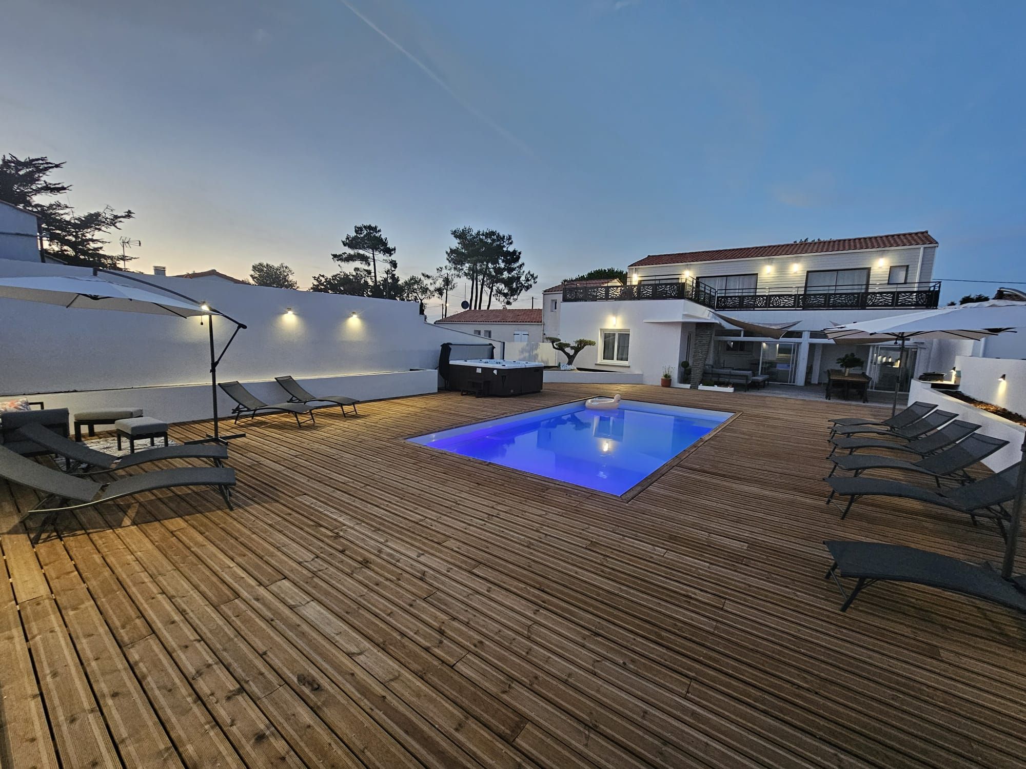 Una terraza de madera con piscina, sillas de descanso y sombrillas.