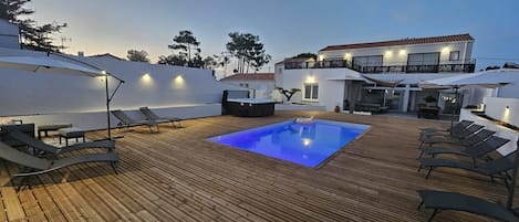 Una terraza de madera con piscina, sillas de descanso y sombrillas.