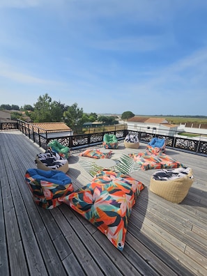 A wooden deck with colorful cushions and a view of the countryside.