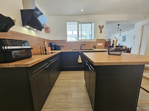 A modern kitchen with dark cabinetry, a wooden countertop, a built-in oven, and a large island with a sink.