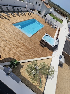 A rooftop with a swimming pool, lounge chairs, and a hot tub.