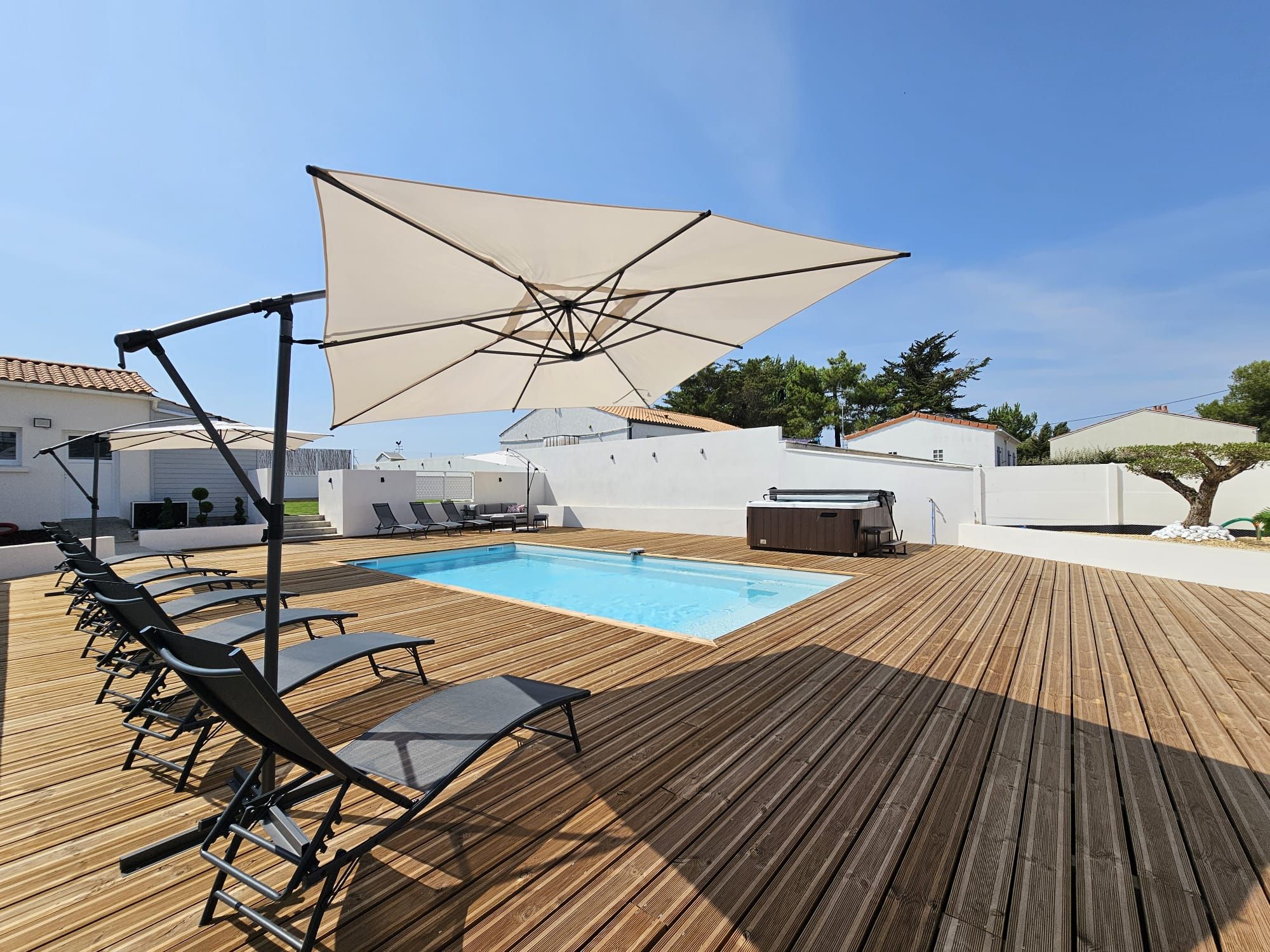 Une terrasse en bois avec une piscine, des chaises longues et des parasols.