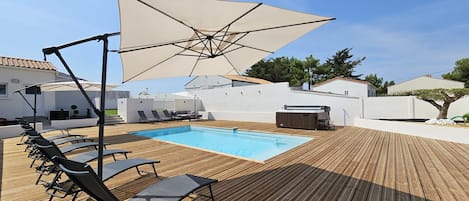 Una terraza de madera con piscina, sillas de descanso y sombrillas.