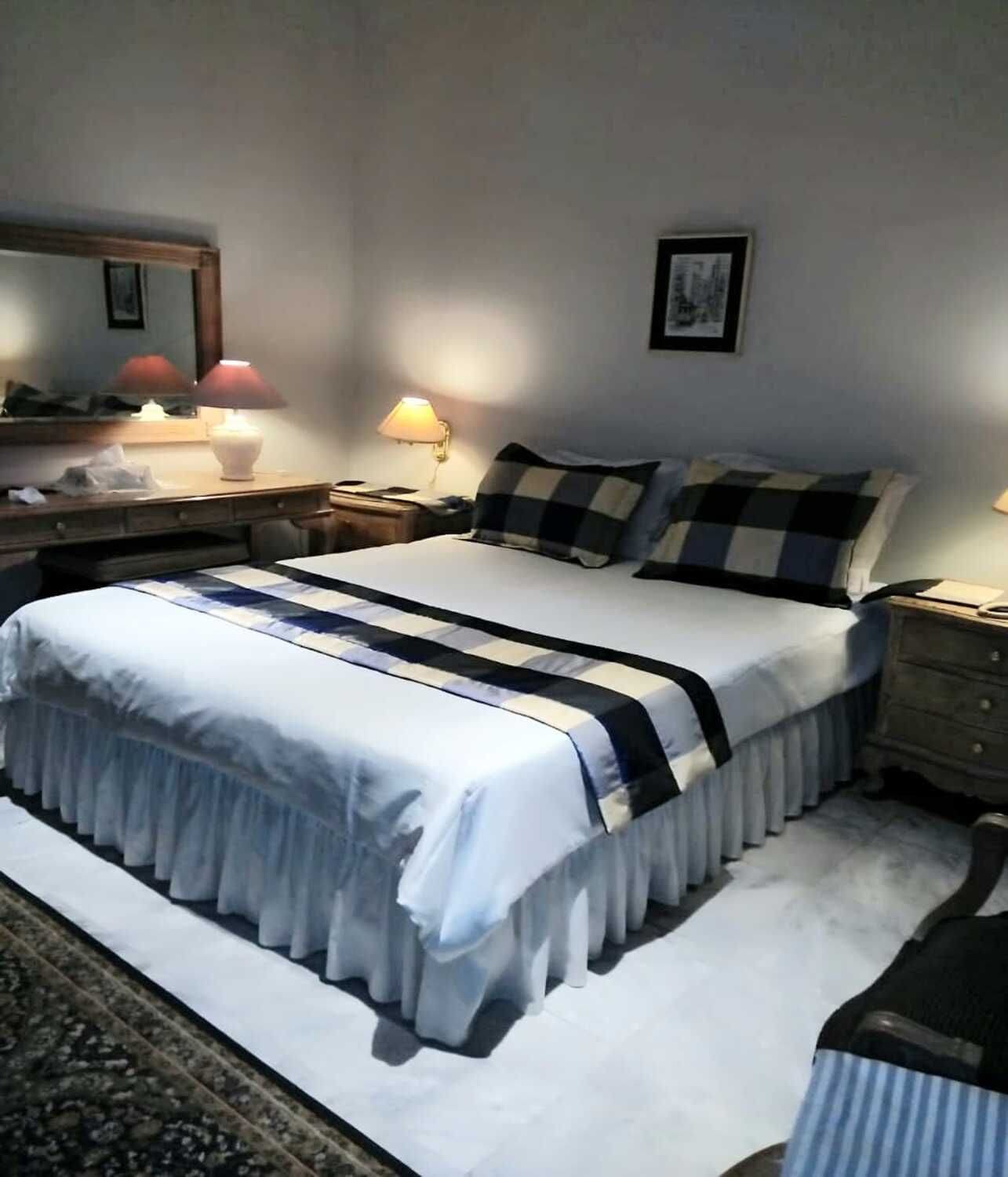 Een bed met een deken met witte en blauwe strepen, een nachtkastje met een lamp, en een nachttafeltje met een lamp.