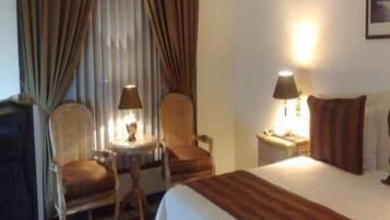 A hotel room with a bed, two chairs, a small table, a lamp, and a nightstand.