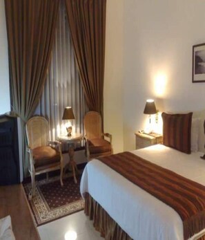 A hotel room with a bed, two chairs, a small table, a lamp, and a nightstand.
