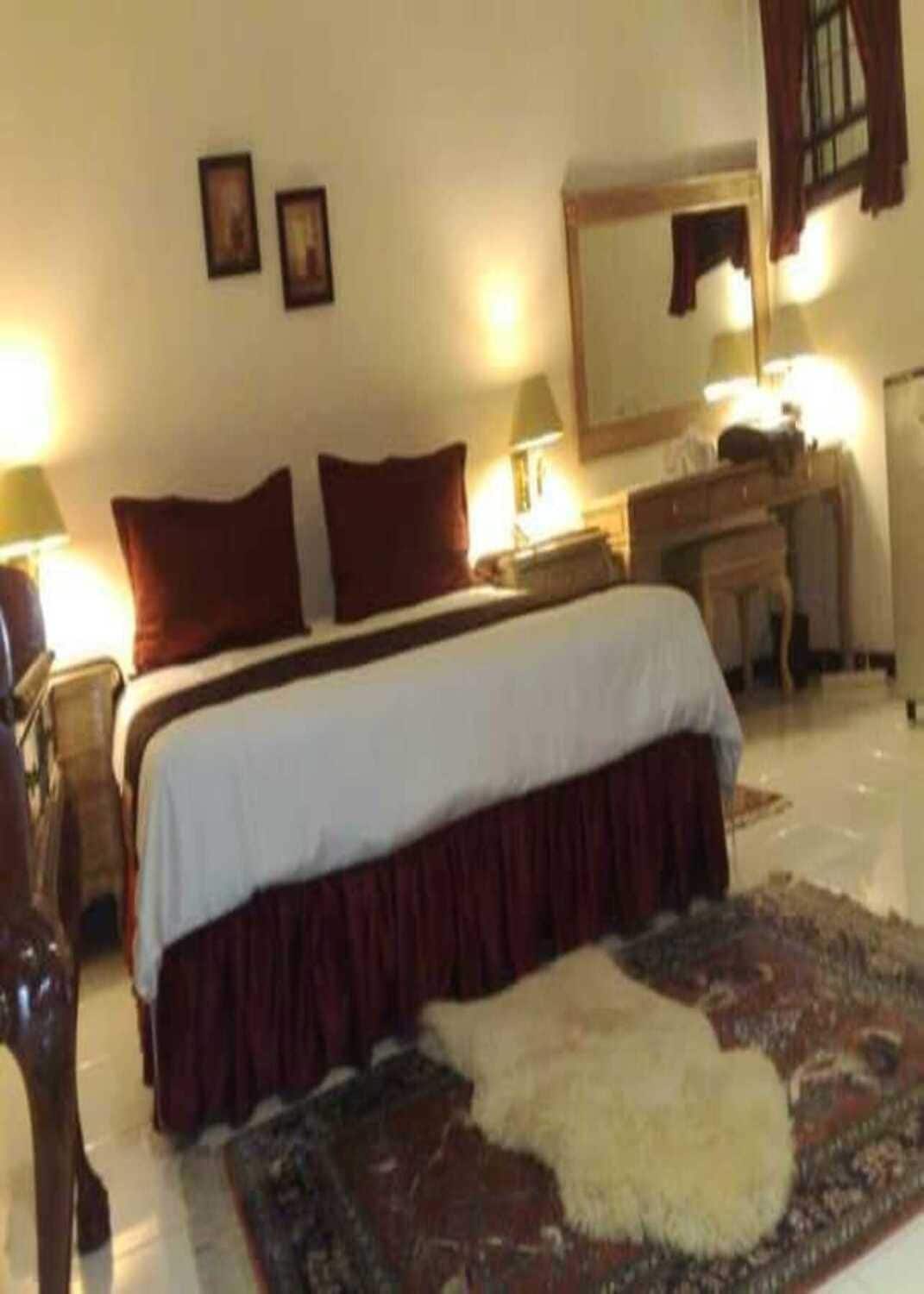 Ein Hotelzimmer mit einem Bett, Nachttischlampen, einem Schminktisch, einem Spiegel und einem Teppich.