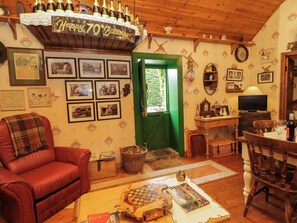A cozy living room with a red leather sofa, a wooden coffee table, and a chessboard. There are framed pictures on the wall, a green door, and a shelf with bottles. - TERESA'S COTTAGE, pet friendly in Bruckless, County Donegal (BRUCKLESS)