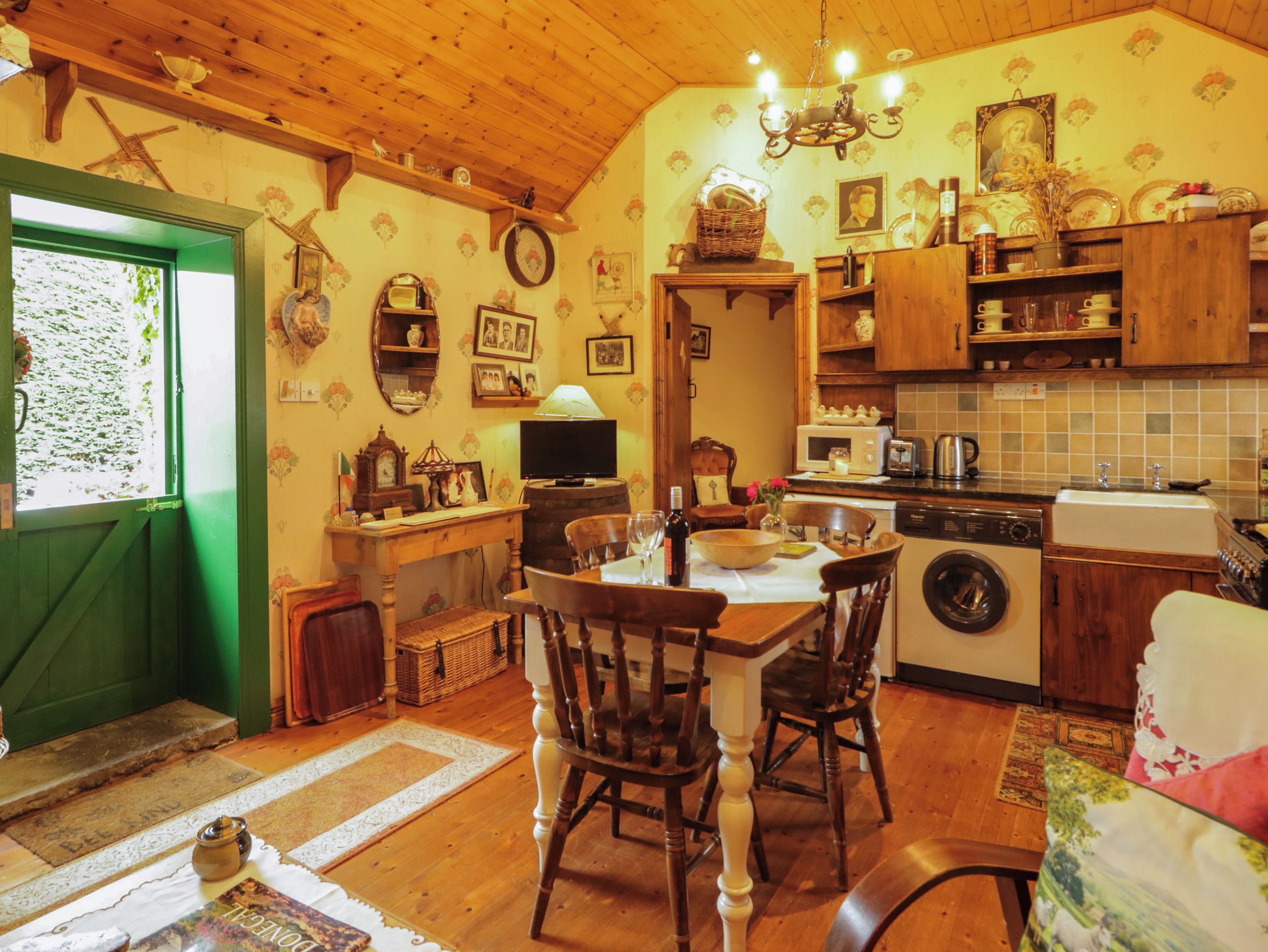 A cozy kitchen with wooden cabinets, a dining table, chairs, a washing machine, and a television.