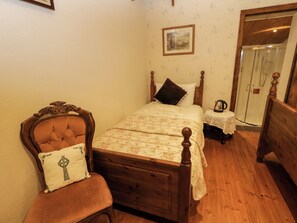 Un dormitorio con una cama de madera, una silla con cojín, una mesita de noche con lámpara y una zona de ducha.