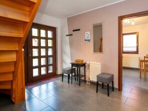 Ein Zimmer mit einer Holztreppe, einer Glastür, einem kleinen Tisch mit Korb, einem Heizkörper und einem Fenster.