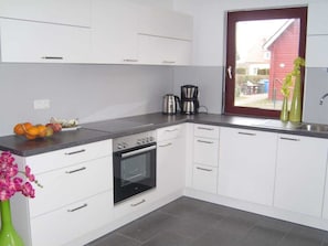 Eine Küche mit weißen Schränken, einem schwarzen Backofen, einer Kaffeemaschine und einem Fenster mit Blick auf ein rotes Gebäude.