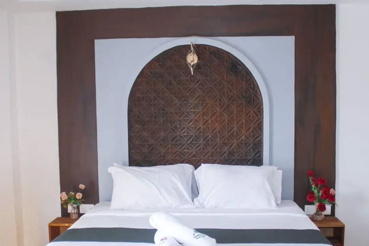A hotel room with a large bed, a wooden headboard, and a decorative wall panel.