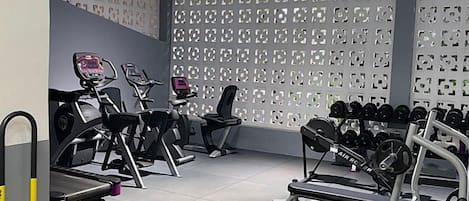 Un gimnasio con equipo de ejercicio, una pared con diseño decorativo y un techo con tragaluces.