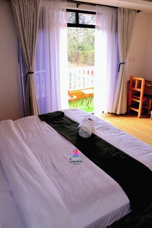Una cama bien hecha con una toalla, una silla de madera y vistas a un espacio exterior a través de una ventana con cortinas.