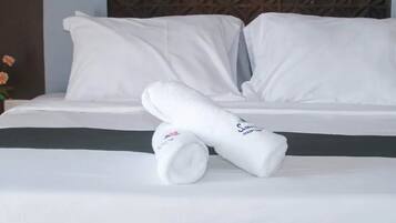 Una cama bien hecha con sábanas y almohadas blancas, una toalla enrollada y un cabecero de madera con un diseño geométrico.
