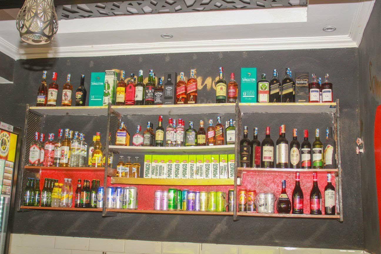 A bar with shelves stocked with various bottles and cans, including spirits and sodas.