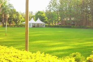 A well-maintained lawn with a white tent structure in the background, surrounded by trees and greenery. - Samarine Resort & Spa Maragua (Maragua)