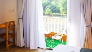 A hotel room with a bed, a wooden chair, a small table, and a balcony with a view of greenery. - Samarine Resort & Spa Maragua (Maragua)