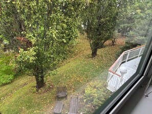 Blick aus einem Fenster auf eine begrünte Fläche mit Bäumen und eine Holzterrasse.