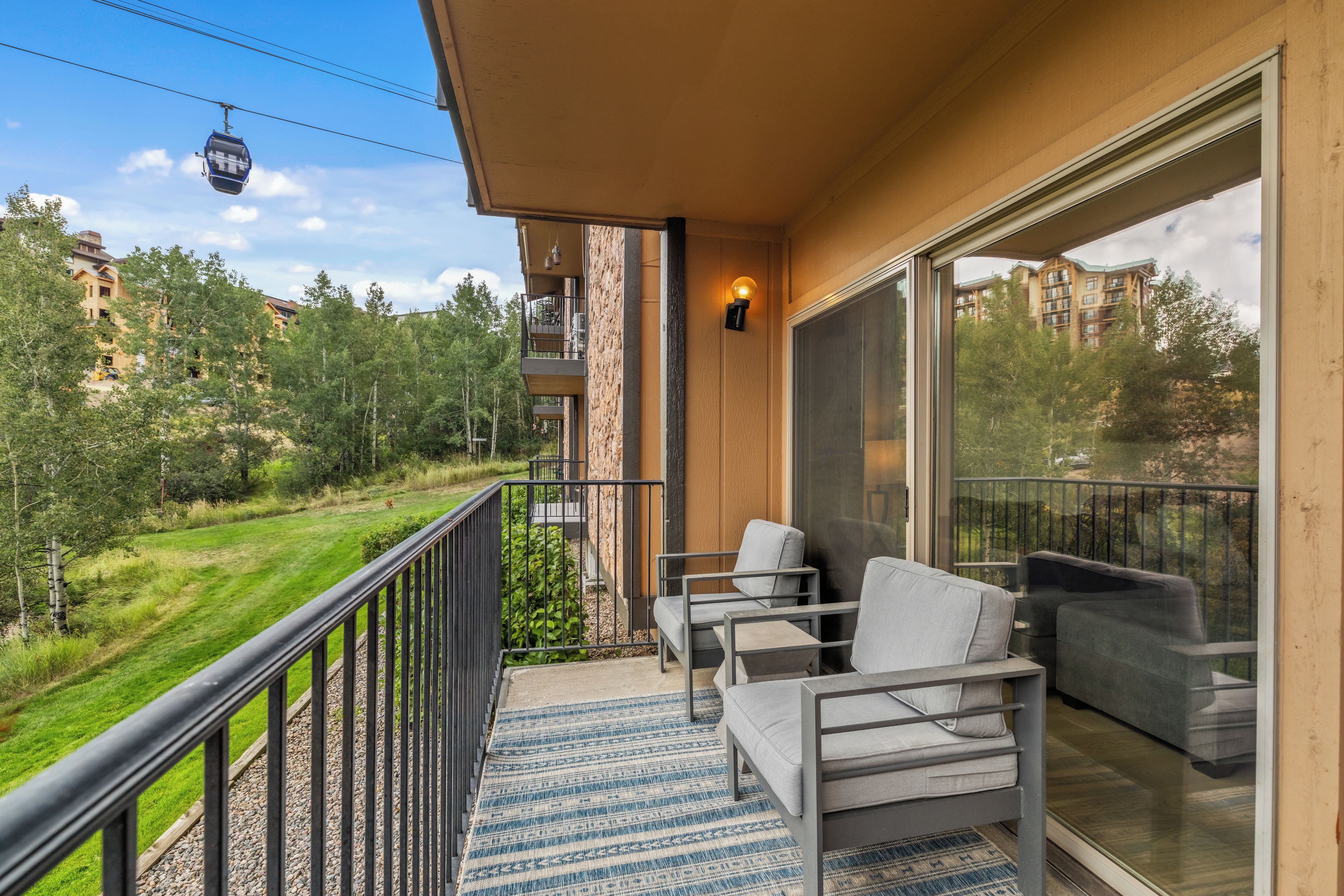 A balcony with a view of a green landscape, a chair, a sofa, and a wall-mounted light fixture.