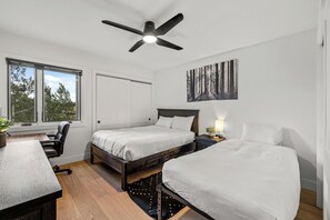 A bedroom with two beds, a desk, a chair, a ceiling fan, and a window with a view of trees. - Ski-In/Out Gondola Views | Fireside & Hot Tubs (Steamboat Springs)