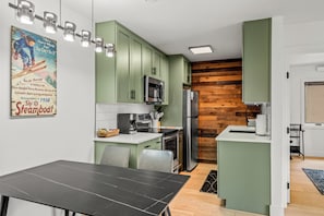 A modern kitchen with green cabinets, a stainless steel refrigerator, and a wooden accent wall. - Ski-In/Out Gondola Views | Fireside & Hot Tubs (Steamboat Springs)
