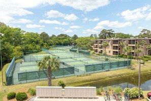 Ein Tennisplatzkomplex mit mehreren Plätzen, umgeben von Grünflächen und einem Gewässer.