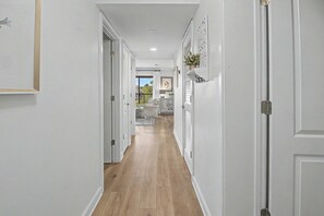 Ein Flur mit Holzdielen, weißen Wänden und einer Tür zu einem Balkon mit Blick.