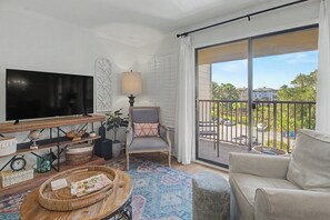 Ein modernes Wohnzimmer mit Fernseher, bequemen Sesseln, einer Couch, einem Couchtisch und einem Balkon mit Blick auf die Nachbarschaft.
