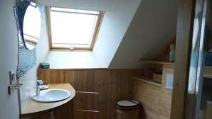 Un bagno piccolo con tetto spiovente, un lucernario, mobili in legno, un lavandino bianco e un water.