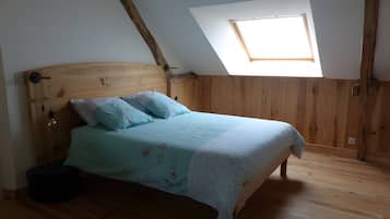 Een slaapkamer met een schuine kap, een dakraam, een houten bed en een nachtkastje.