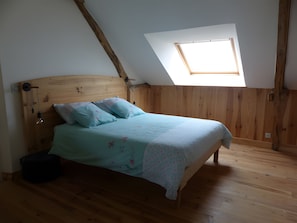 Un dormitorio con techo inclinado, tragaluz, estructura de cama de madera y una mesita de noche.