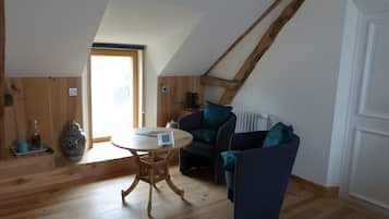 A cozy loft-style room with a sloped ceiling, wooden flooring, a round table, and a dark blue sofa with teal cushions.