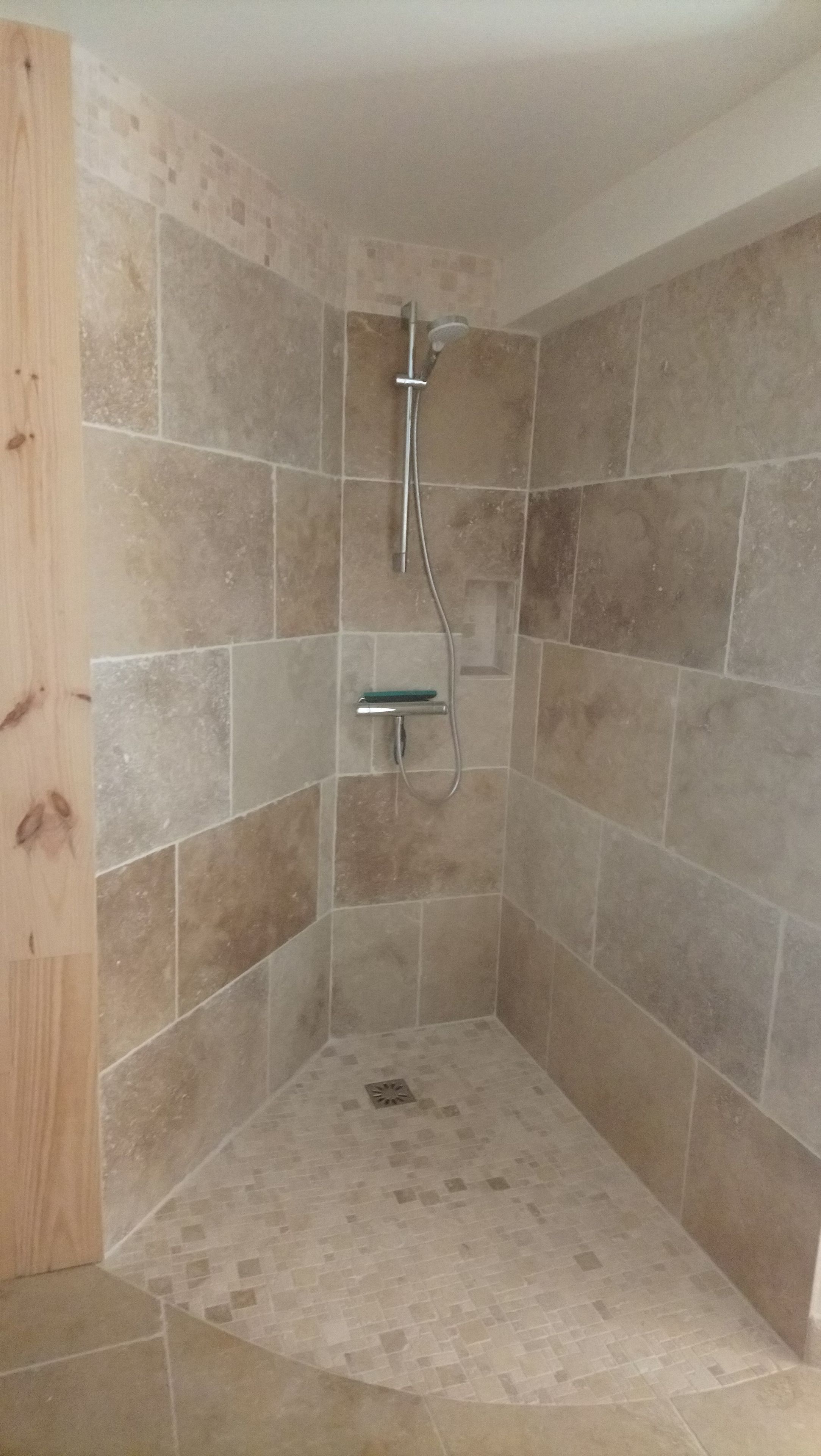 Ein Duschbereich mit gefliesten Wänden und Boden, einer Handbrause und einem an der Wand montierten Wasserhahn.