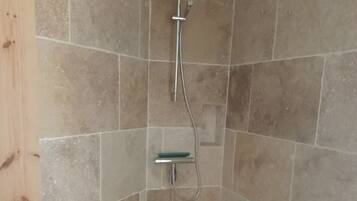 Ein Duschbereich mit gefliesten Wänden und Boden, einer Handbrause und einem an der Wand montierten Wasserhahn.