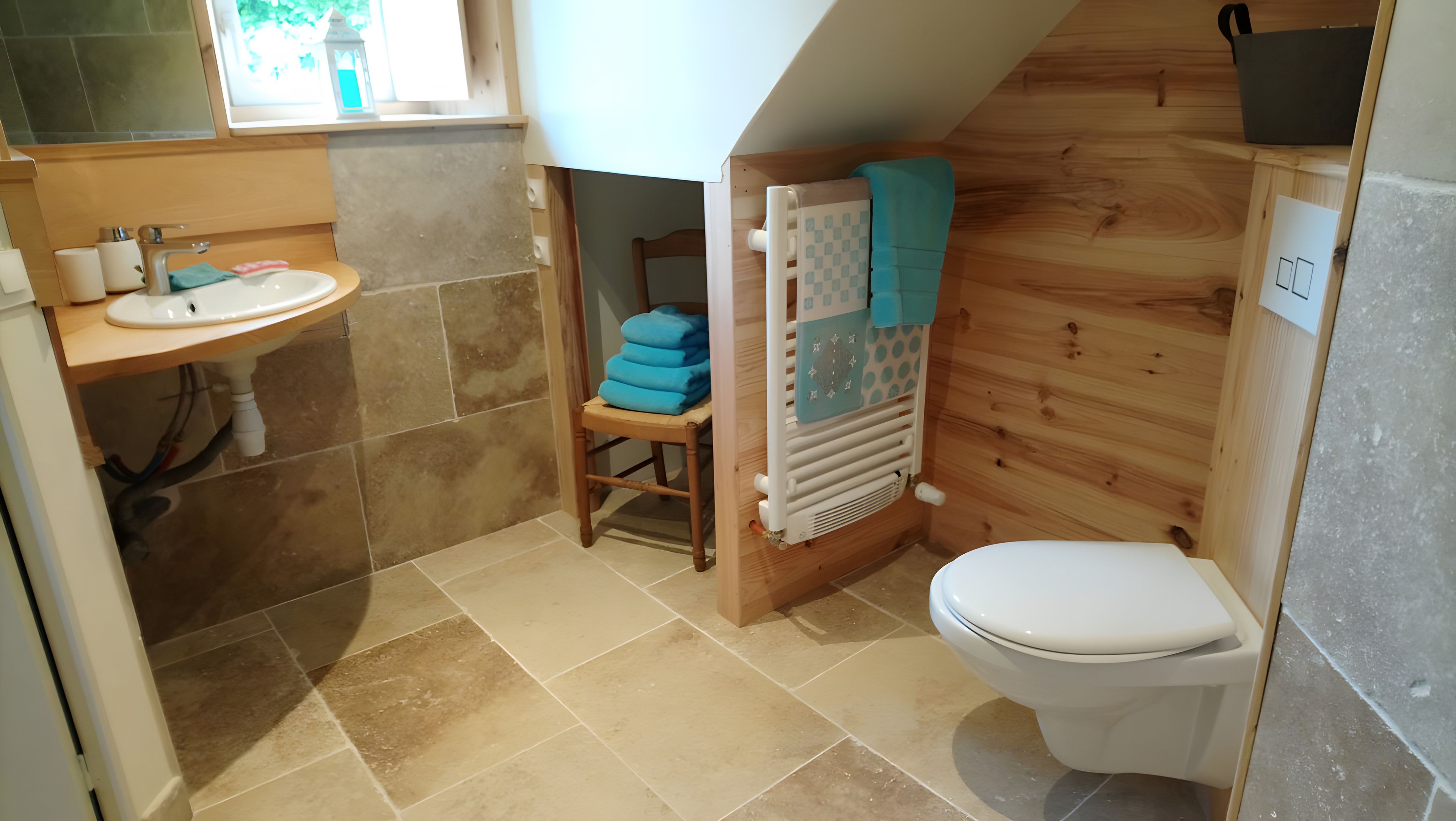 Baño pequeño con lavamanos, inodoro y una silla con toallas dobladas.