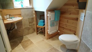 A compact bathroom with a sink, toilet, and a chair with folded towels.