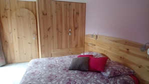 A bedroom with a wooden wardrobe, a bed with patterned bedding, and a nightstand with a lamp. - Bed and Breakfast 'Chambre D'hôtes Bois De Rose' with Private Garden and Wi-Fi (La Hoguette)