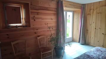Ein Zimmer mit Holzwänden, einem Fenster, einem Stuhl, einer Zimmerpflanze und einem Bett.