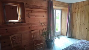 A room with wooden walls, a window, a chair, a potted plant, and a bed.